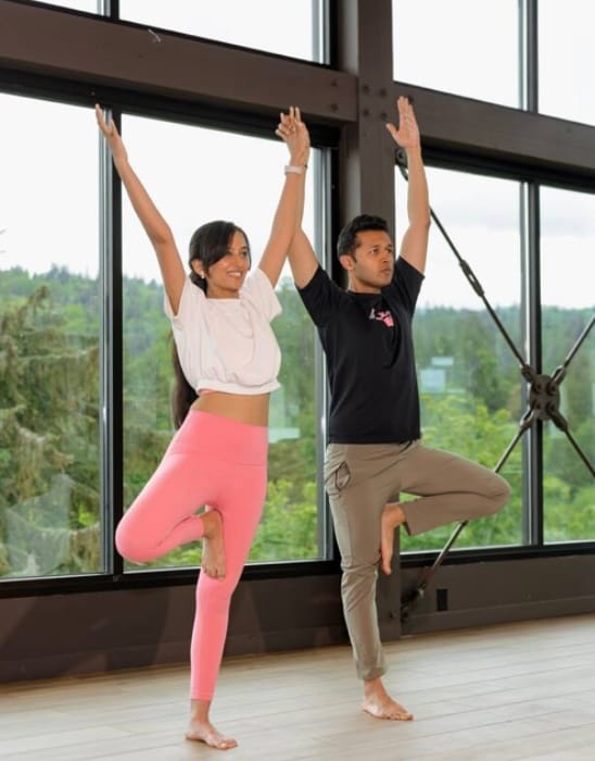 Partner yoga session with arms raised in modern studio with mountain views